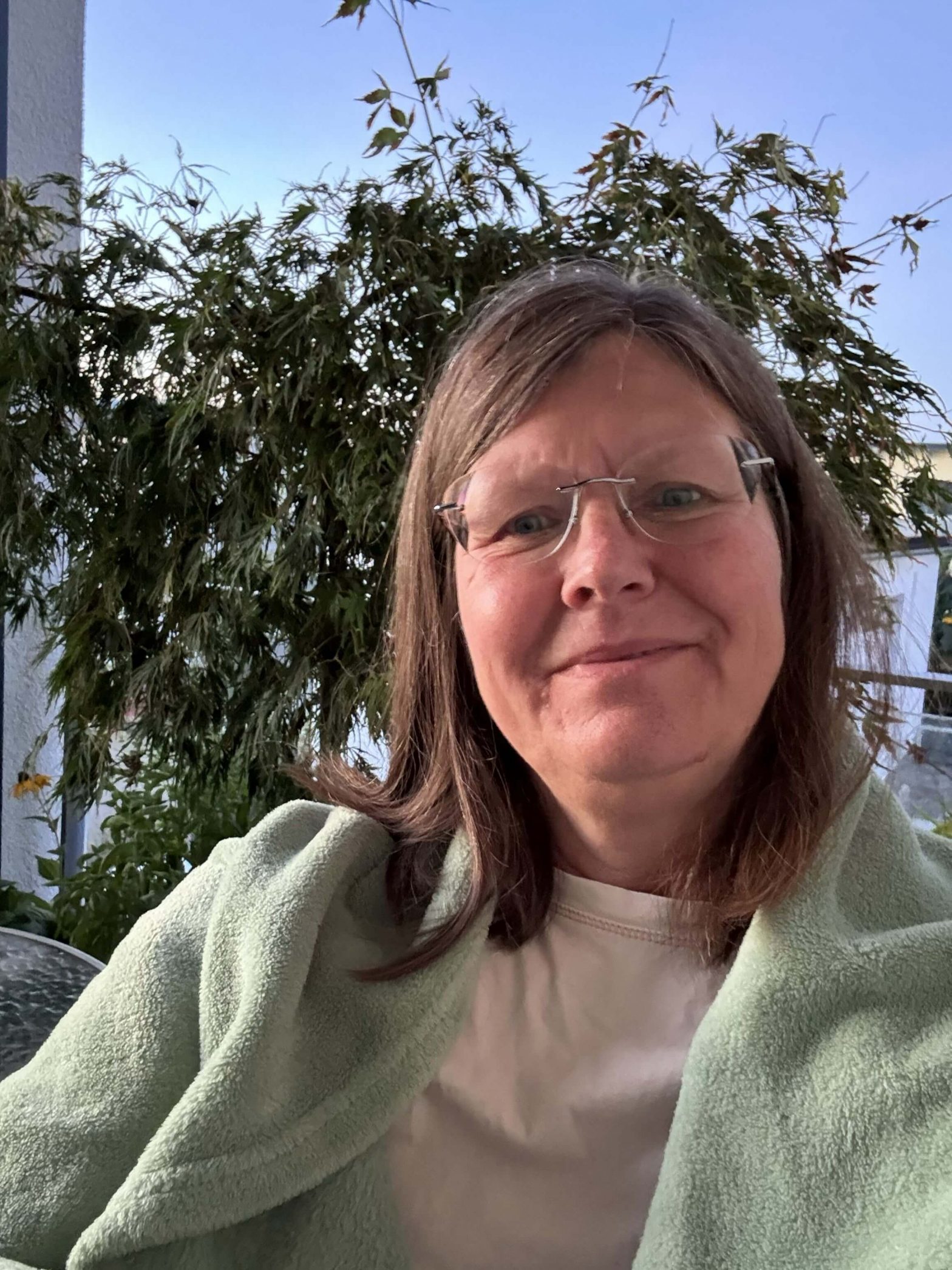 Eine Frau sitzt eingekuschelt auf einem Balkon und lächelt warm in die Kamera.