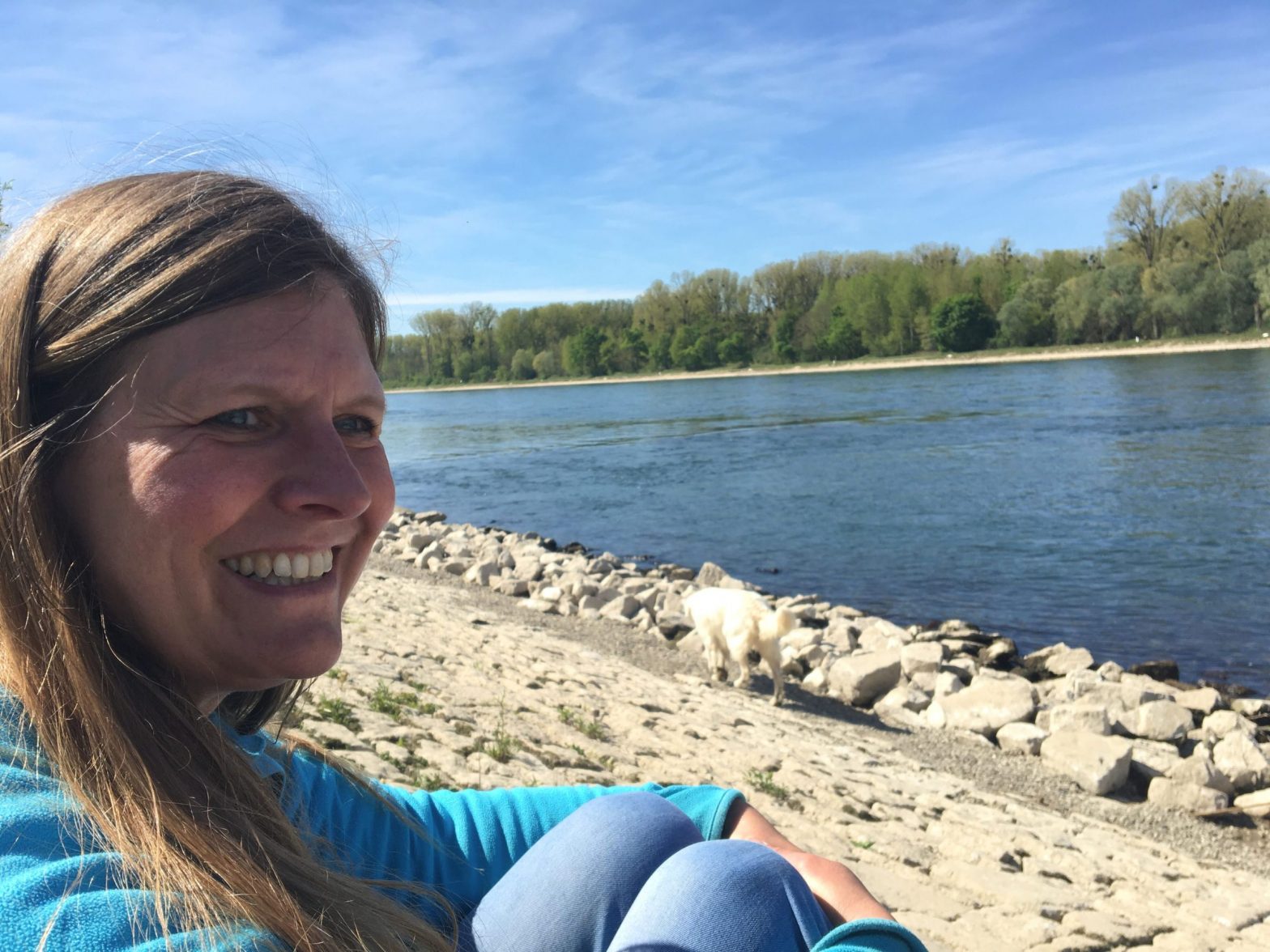 Frau sitzt am Flussufer und blickt nachdenklich lächelnd zur Seite.